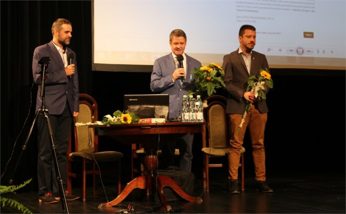 Obraz zawiera 3 osoby na scenie. Stoją na niej dr Dominik Wróbel, prof. Grzegorz Przebinda i mgr Igor Przebinda