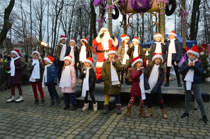 Obraz zawiera: Mikołaj wśród śpiewających dzieci na tel glorietki w parku miejskim w Jaśle