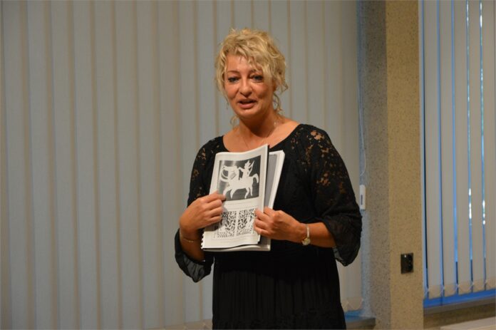 Kobieta trzyma w ręku ksiązkę z rysunkiem, ktory pokazuje odbiorcom.
