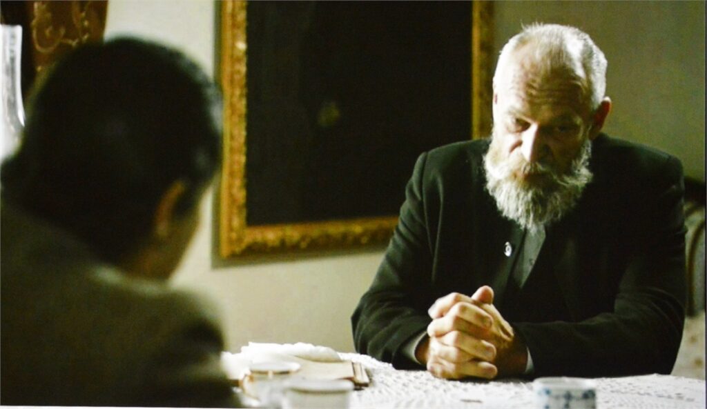 Obraz zawiera: dwóch mężczyzn siedzi naprzeciwko siebie przy stole. Kadr z filmu, Łukasiewicz, nafciarz romantyk.