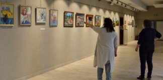 Jury oceniało prace w IX Biennale Sztuki Ludowej i Nieprofesjonalnej Na ścianie powieszona są obrazki, przed nimi stoją dwie kobiety -jurorki. Pierwsza od lewej stoi tyłem i pokazuje drugiej lewą ręką jedną z prac
