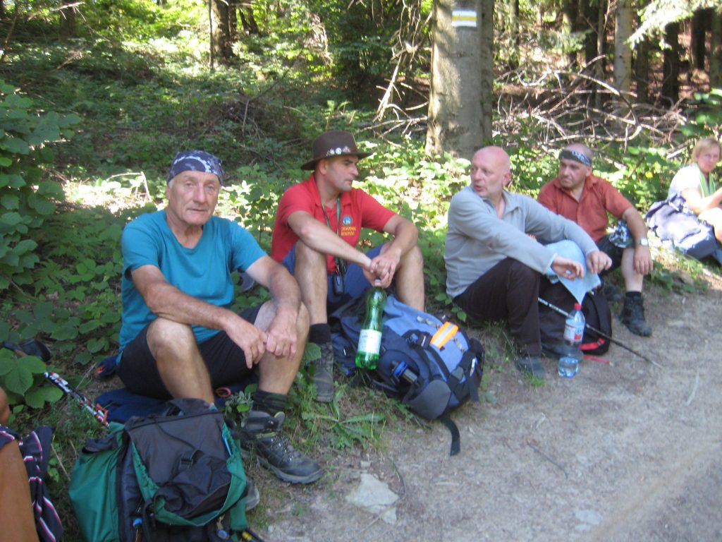 Czterech mężczyzn siedzi na trawie przy leśnej drodze i odpoczywają. dwóch w środku rozmawia ze sobą