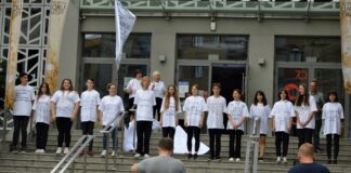 Miłość jest  poezją…spektakl uliczny na schodach jasielskiego domu kultury stoją uczestnicy warsztatów ubrani w białe koszulki zapisane cytatami Baczyńskiego. W tle dwie kobiety ubrane w białe koszulki oraz mężczyzna ubrany w szara koszulę. Na dole schodów stoją kamerzyści, nagrywają ujęcia do filmu