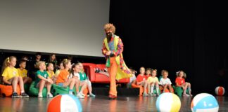 Akademia Pana Kleksa na jasielskiej scenie Grupa dzieci siedzi na czarnej podłodze, obok leżą duże dmuchane kolorowe piłki. Po scenie chodzi kolorowo ubrany dorosły mężczyzna
