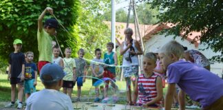 Magiczny przystanek w Żółkowie Przy dużym szachowym stole znajduje się trzech małych chłopców, nieopodal nich innych chłopiec robi duże banki mydlane. Przygląda się temu grupka dzieci oraz jedna kobieta