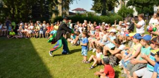 Na starym jarmarku Klaun podbiega do grupy dzieci i zaprasza do zabawy. Dzieci siedzą na ławkach