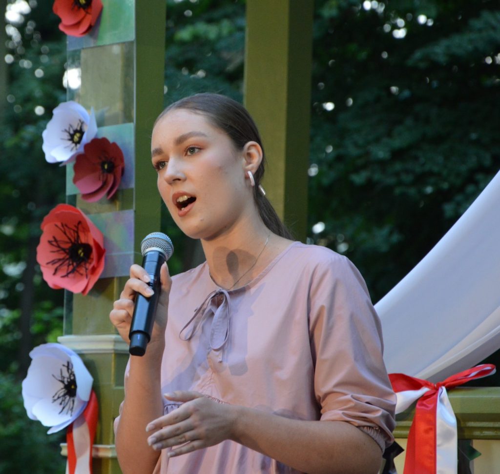 Uczestniczka konkursu niepodległa, niepokorna śpiewa przed glorietką w parku miejskim piosenkę