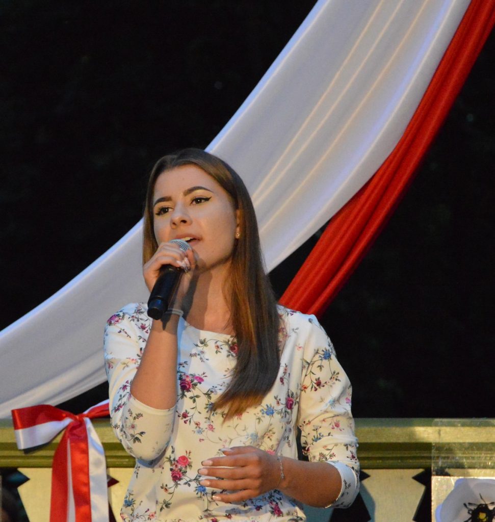 Uczestniczka konkursu niepodległa, niepokorna śpiewa przed glorietką w parku miejskim piosenkę