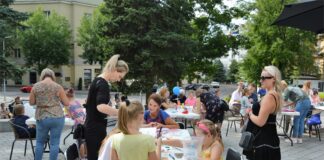 Jasielski Weekend z Kulturą Dzieci koloruja rysowanki przy stolikach na tarasie Jasielskiego Domu Kultury. Rodzice pomagają im w tych pracach