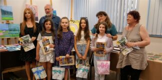 W JDK: Wystawa powarsztatowa czworo nagrodzonych dzieci i czworo dorsłych pozuje do zdjęcia z dyplomami. W tle za nimi stoły z pracami palstycznymi.