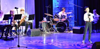 Kolędowe nagrody dla wokalistów i zespołu JazzKids z JDK Na scenie jasielskiego domu kultury występują młodzi artyści, uczestnicy dwudziestego siódmego konkursu kolęd i pastorałek na nutę kantyczek. Na pierwszym planie jest młody chłopiec z mikrofonem, za nim gra zespół muzyczny na instrumentach