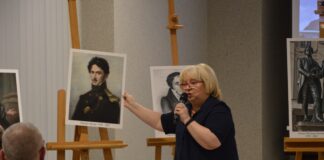 Historyczne przenikanie kultur Obraz zawiera: Kobieta z mikrofonem prezentuje przybyłym podobiznę jednego z twórców romantycznych.