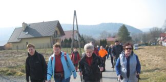 Obraz zawiera: Grupe ludzi z kijkami wędrujących przez wieś