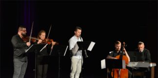 Vivaldi poznawany Obraz zawiera: pięć osób na scenie JDK: czterech mężczyzn i kobieta. Stoją: skrzypek, skrzypaczkai klarnecista, siedzą przed swoimi instrumentami: kontrabasista i organista