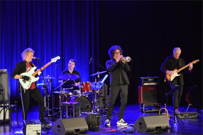 Morrison Tres i Christoph Titz_2 Obraz zawiera: czterech muzyków na scenie JDK. Przed nim dwa głośniki odsłuchowe. Muzyk od lewej z długimi siwiejącymi włosami gra w specjalnych rękawiczkach na gitarze elektrycznej. Pomiędzy nim, a trębaczem, nieco z tyłu gra perkusista. Z prawej strony czwarty muzyk składu gra na gitarze basowej, która podpięta jest do stojącego za nim wzmacniacza.