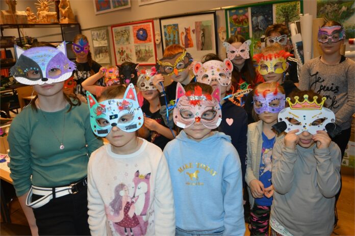 Maski Karnawałowe w JDK_4 Obraz zawiera: Kilkanaścioro dzieci ubrane we własnoręcznie wykonane maski karnawałowe prezentuje swoje dzieła. Z przodu stoją cztery kotki, a z tyłu misie, sowy, pawie czy motylki.