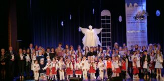 Kolędy Podkarpacia zabrzmiały w Jasielskim Domu Kultury Obraz zawiera: Wszyscy finaliści Koncertu "Na Nutę Kantyczek - Kolędy Podkarpacia", stoją na scenie wraz z jurorami, mecenasami kultury, dyrektor JDK oraz zastępcą burmistrza Jasła, Elwirą Musiałowicz - Chech i śpiewają wspólnie kolędę. Za nimi scenografia koncertu czyli wielki, biały anioł, duże podłużne okno, duże płatki śniegu oraz z prawej strony zwisający z góry baner z napisami "Na nutę kantyczek".