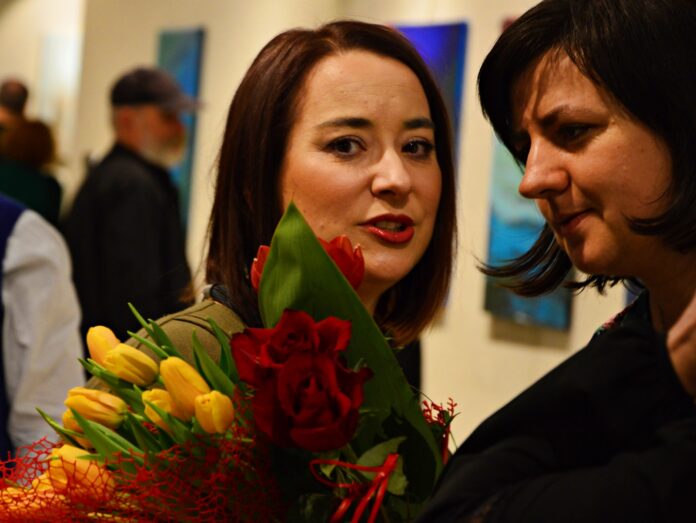 DSC_1849 Na pierwszym planie od lewej Patrycja Dyląg, autorka wystawy, trzyma bukiet kwiatów rozmawia z uczestniczką wystawy