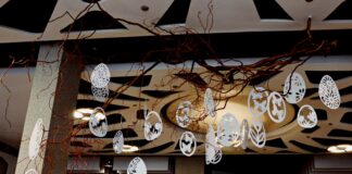 Aktywnie i pożytecznie Pod ozdobnym sufitem w holu jasielskiego domu kultury wiszą przyczepione do gałęzi ręcznie robione pisanki z białego papieru. Obok szary filar, w tle widoczne światła sufitowe