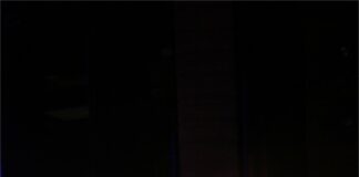 Obraz zawiera: Na pierwszym planie saksofonista grający na saksofonie. Przed nim stoi pulpit na nuty. Z lego lewej strony w oddali perkusista za zestawem perkusyjnym.