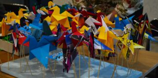 Kolorowe żurawie witają gości JDK Na stole leży duży kawałek styropianu w kształcie prostokąta. do niego są wpięte na patykach kolorowe żurawie