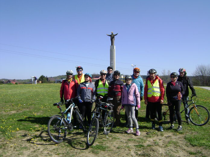 Na tle pomnika Jezusa pozują do zdjęcia uczestnicy wycieczki rowerowej. Jest piękna słoneczna pogoda, bezchmurne niebo