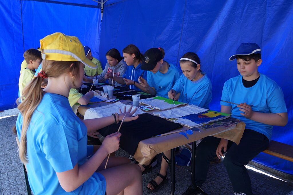 Grupa dzieci w niebieskim namiocie maluje rysunki. 