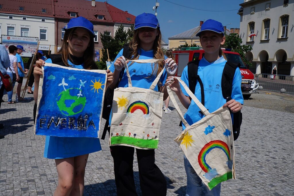 Trzy radosne dziewczynki pozują do zdjęcia. W rękach trzymają duże, kolorowe torby ekologiczne.