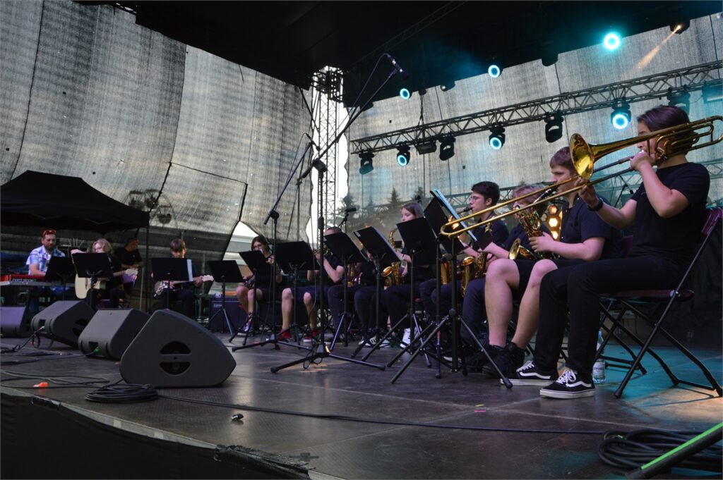 Obraz zawiera: 12 młodych muzyków grupa Jazz of Combo siedzi i gra na instrumentach na scenie. Pierwszy z lewej za klawiszami siedzi założyciel formacji Wojtek Nowicki, instruktor muzyki w JDK.