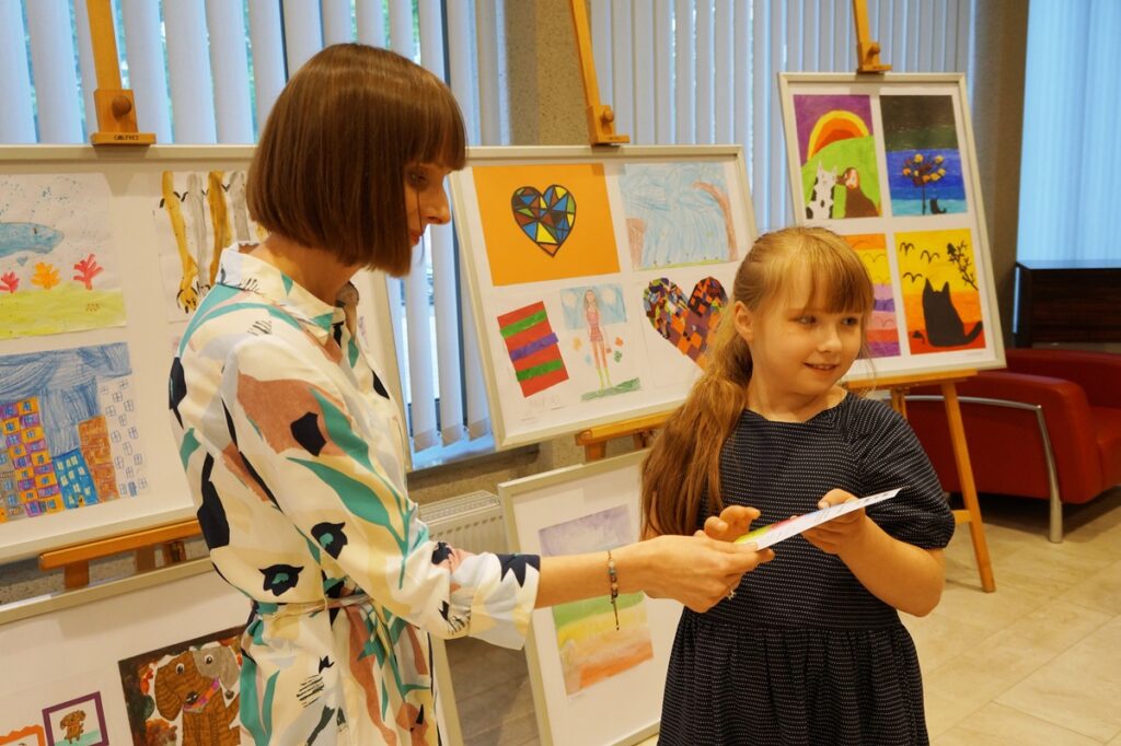 Pani Kasia, plastyczka wręcza dziewczynce pamiątkowy dyplom ukończenia zajęć plastycznych.