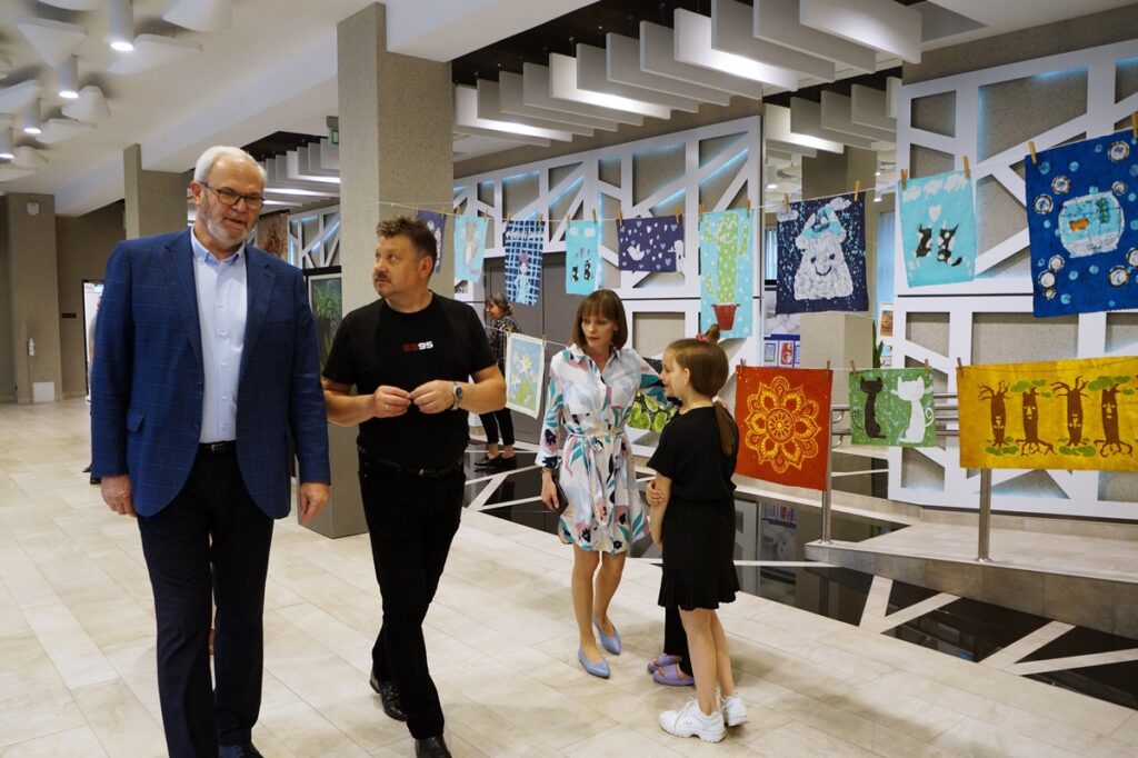Pięć osób: dwóch dorosłych mężczyzn, dorosła kobieta i dwójka radosnych dzieci. Wszystkie z osób prowadzą między sobą rozmowę.