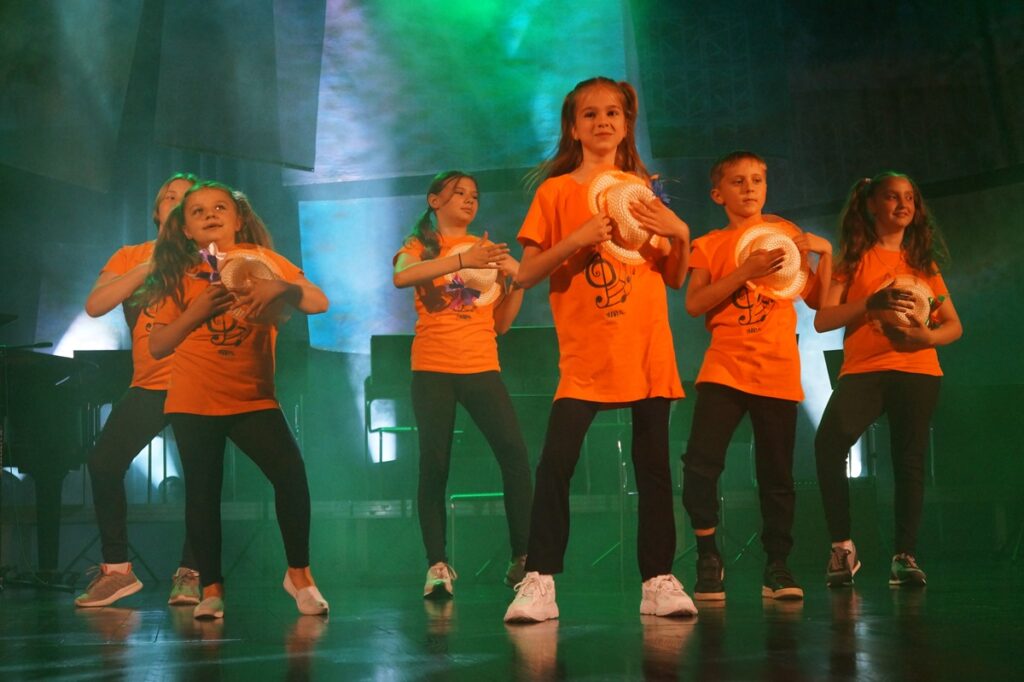 Grupa dzieci tańczy na scenie.