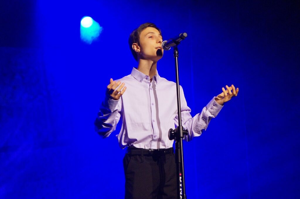 Młody chłopak śpiewa na scenie. 
