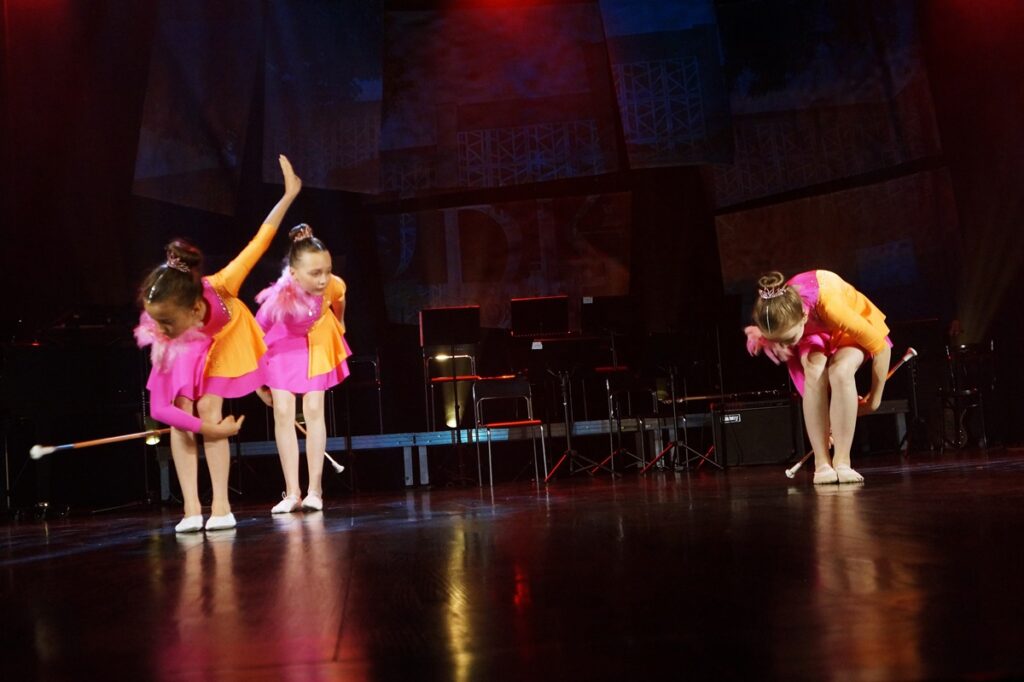 Trzy dziewczynki: mażoretki, które wykonują układ choreograficzny.