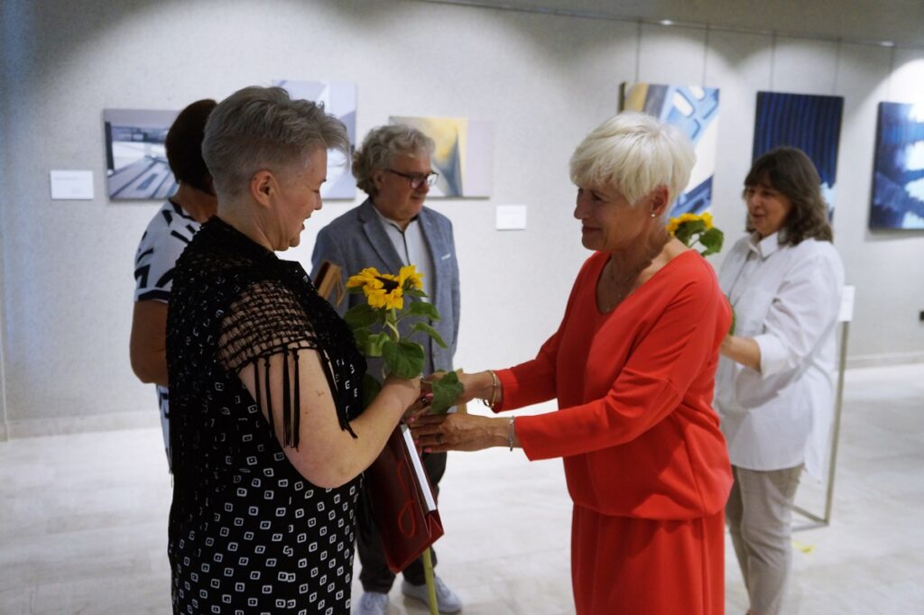 Pięć osób: cztery kobiety i jeden mężczyzna. Dwie kobiety, a więc Pani Anna Brożyna, plastyk i Pani Helena Gołębiowska, dyrektor Jasielskiego Domu Kultury, wręczają zaproszonym artystom, przepiękne, duże żółte słoneczniki. 