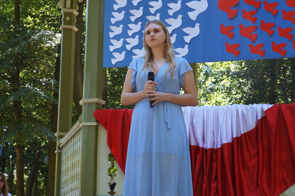 Młoda dziewczyna, w pięknej niebieskiej sukience, śpiewa na scenie.