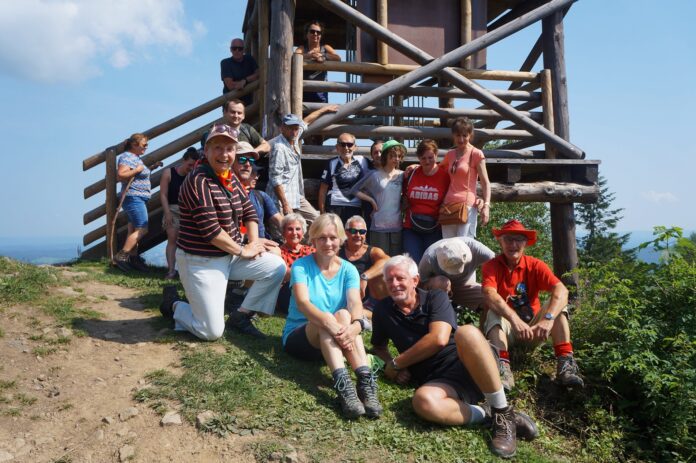 Grupa radosnych turystów przed wieżą widokową na górze Korbania.