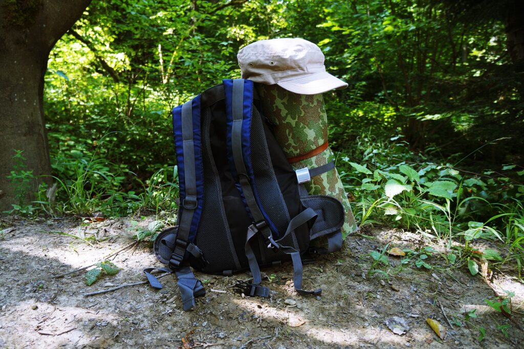 Stojący na górskim szlaku: plecak wraz z beżową czapką i składaną matą. 