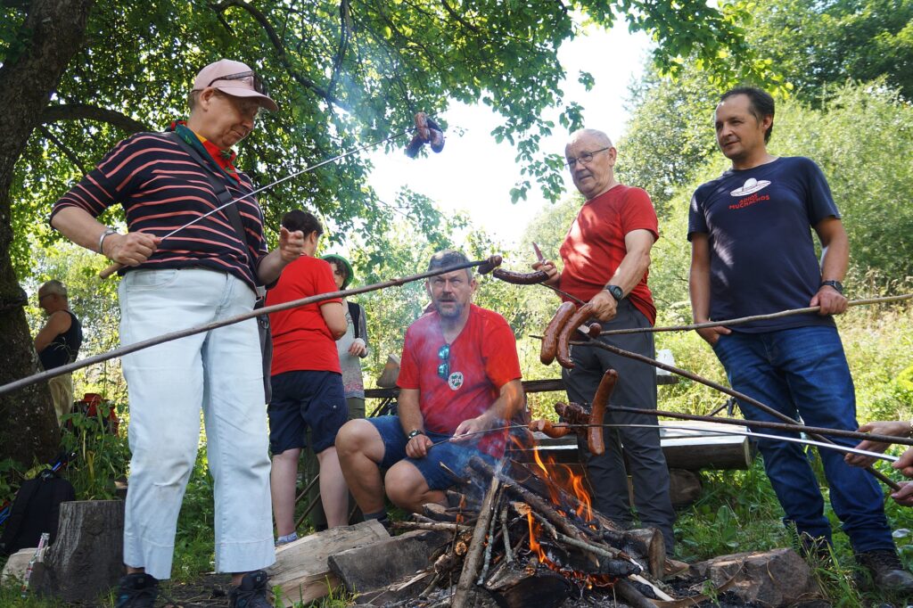 Grupa turystów piecze kiełbaski. 