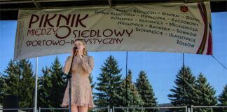 Obraz zawiera: Na scenie śpiewa do mikrofonu na statywie wokalistka JDK - Laura Gondek. Blondwłosa nastolatka trzyma oburącz mikrofon, ma lekko przymknięte oczy. Na sobie jasna sukienkę do kolan z rękawami.