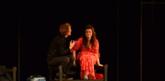 Obraz zawiera: Kobieta i mężczyzna siedzą na oparciu ławki dworcowej, z nogami na siedzisku. Mężczyzna gestykuluje zwrócony w stronę kobiety,