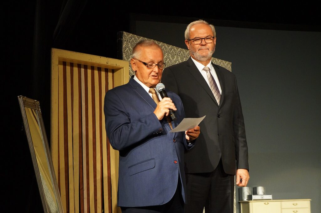 Na scenie stoi dwóch mężczyzn: Ryszard Pabian – burmistrz Jasła i Sławomir Piotrowski - przewodniczący Rady Seniorów. Sławomir Piotrowski przemawia do mikrofonu.