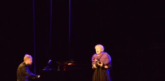 Na scenie jasielskiego domu kultury występują starsza kobieta i młody mężczyzna. On ubrany na czarno akompaniuje na fortepianie, kobieta natomiast w czarnej sukni i fioletowym szalu, ozdobionym z przodu kwiatami wykonuje arie operowe. Kobieta ma jasnoblond włosy upięte w kok, mężczyzna modną, postrzępioną ciemnoblond czuprynę