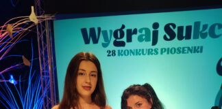 Wielkie brawa dla Karoliny Na tle napisu Wygraj sukces stoi Karolina Polak w czarnej sukience w duże czerwone kwiaty, przed sobą trzyma dyplom. Obok niej niska kobieta, brunetka z długimi włosami, spiętymi w kucyk, ubrana na czarno w marynarkę i spodnie