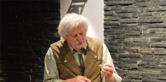 Historie zatrzymane w zegarkach Obraz zawiera: Gość Klubu Ludzi z Pasją, ubrany w koszulę i kamizelkę myśliwską, prawą ręka wskazuje na trzymany w lewej ręce zegarek kieszonkowy.