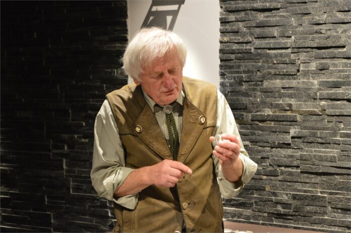 Zegarki_4 Obraz zawiera: Gość Klubu Ludzi z Pasją, ubrany w koszulę i kamizelkę myśliwską, prawą ręka wskazuje na trzymany w lewej ręce zegarek kieszonkowy.