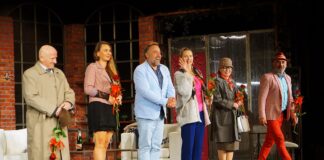 Grupa aktorów stoi na scenie. Każdy artysta trzyma w dłoni czerwoną różę.