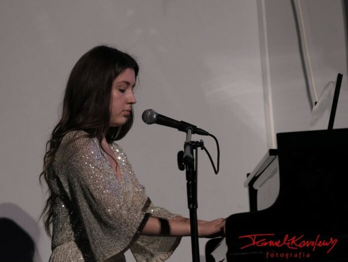 Obraz zawiera: Karolina Polak akompaniuje sobie na fortepianie podczas występu wokalnego.