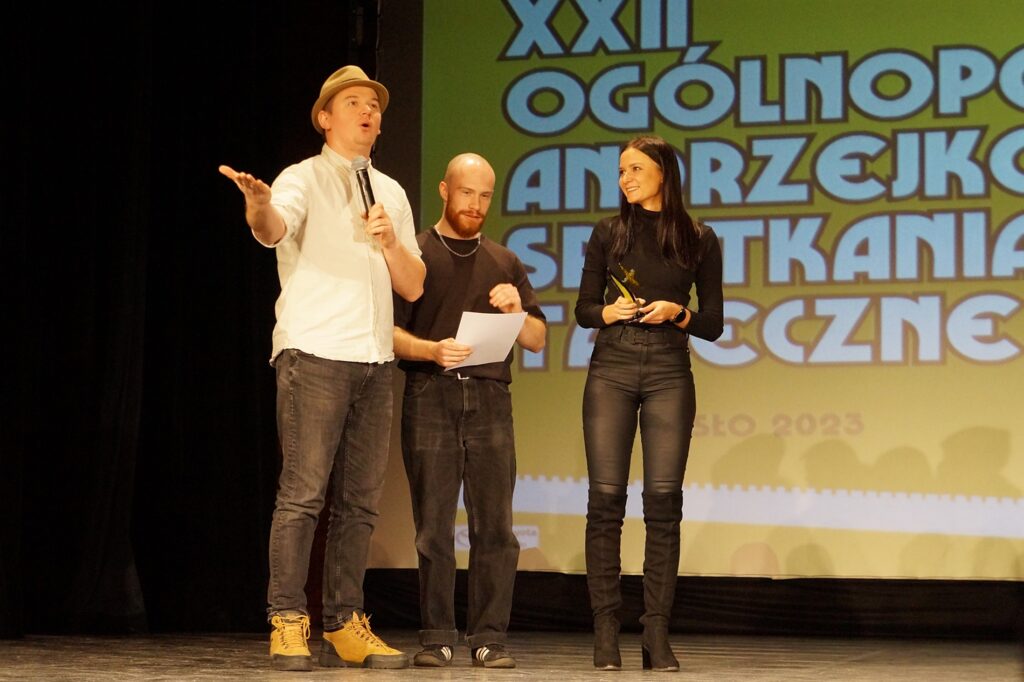 Na scenie stoją trzy osoby: dwóch mężczyzn i kobieta. Jury ogłasza werdykt.