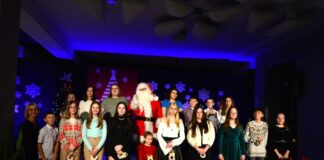 Obraz zawiera: Wspólne zdjęcie młodych wykonawców i instruktor śpiewu Kateryny Kryvoruchko ze Świętym Mikołajem.